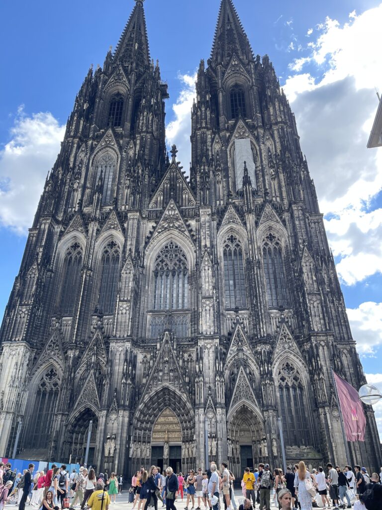 Bild vom Kölner Dom, der von unten betrachtet wird, im Hintergrund blauer Himmel mit ein paar Quellwolken